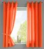 Two orange curtains are hanging on a window rod, with one curtain tied back with a fabric tie. Produktbild-Vorschau