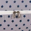 A close-up view of a gray fabric with a navy blue star pattern, featuring two silver zippers. Náhled obrázku produktu