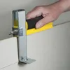 A hand is holding a drywall scoring tool against a wall. Náhled obrázku produktu