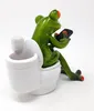 A decorative figurine of a green frog sitting on a toilet and looking at a smartphone. Produktbild-Vorschau