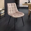 A plush, tufted dining chair in a champagne-greige velvet is shown in a modern dining room setting with dark wood floors and a wooden dining table in the background. Produktbild-Vorschau