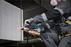 A person wearing protective gear is using a cordless angle grinder to cut a concrete block. Náhľad obrázku produktu