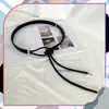 A black leather belt with gold accents is laid out on a white surface, possibly a bed or table, with an open book underneath. Náhled obrázku produktu