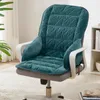 A teal colored chair cushion with a quilted pattern is placed on a grey office chair. The chair is on a white rug in a room with a plant and a bookshelf in the background. Náhled obrázku produktu