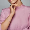 A close-up shot of a woman's arm wearing a silver bracelet with a charm, against a pink top. Podgląd zdjęcia produktu