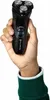 A hand holding a black electric shaver. Voir les images du produit