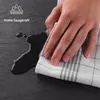 A hand is shown wiping up a spill with a checkered cloth on a dark surface. Anteprima dell’immagine prodotto