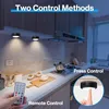 A kitchen counter with under-cabinet lights, a remote control, and a hand pressing a light. Produktbild-Vorschau