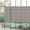 A close-up view of a rattan-look privacy screen installed on a fence, with greenery visible in the background. Produktbild-Vorschau