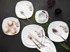 A flat lay of a 30-piece dinnerware set with an orchid motif, arranged with pastries and cutlery on a dark background. Produktbild-Vorschau
