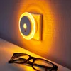 A night light is plugged into a wall outlet, casting a warm amber glow on the textured wall and a pair of glasses on a surface below. Produktbild-Vorschau