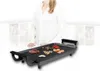 A person is standing behind an electric grill with food on it. Produktbild-Vorschau