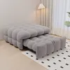 A grey tufted sofa bed is shown in a room with a floor lamp and curtains in the background. Produktbild-Vorschau