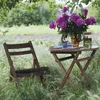 A wooden folding chair sits next to a small wooden table set with a vase of peonies, glasses, and a pitcher of infused water in a grassy outdoor setting. Náhľad obrázku produktu