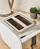 A close-up shot of a white and silver toaster with glowing heating elements, set on a wooden countertop next to two small potted plants. Podgląd zdjęcia produktu