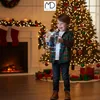 A young boy holds a glowing gift box in front of a decorated Christmas tree and fireplace. Podgląd zdjęcia produktu