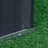 A close-up view of the bottom corner of a dark gray raised garden bed, showing its metal base resting on artificial green grass. Podgląd zdjęcia produktu