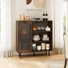 A rustic wooden sideboard with a glass door, filled with dishes, glasses, and decorative items, is placed in a dining room setting next to a window with white curtains. Náhľad obrázku produktu