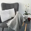 A gray armchair with two white pillows and a gray and white patterned throw blanket. Produktbild-Vorschau