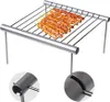 A portable, foldable stainless steel grill with skewers of meat on it, shown from a slightly elevated front-left angle. Two close-up insets show details of the grill's construction. Produktbild-Vorschau