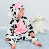 A baby wearing a cow costume sits on a blue rug next to a stuffed lamb. Produktbild-Vorschau