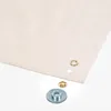 A close-up view of a piece of beige fabric with several grommets and grommet components laid out on a white background. Produktbild-Vorschau