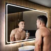 A man is shaving in front of a lit mirror in a modern bathroom. Produktbild-Vorschau