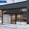 A black awning is extended over the entrance of a store, with a brick wall and a glass door visible. Anteprima dell’immagine prodotto