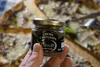 A hand holds a small jar of truffle cream in front of a pizza. Produktbild-Vorschau