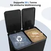 A close-up view of a black dual-compartment trash can with its lids open, showing the interior bins with different types of waste and recycling symbols. Náhled obrázku produktu