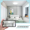A bedroom scene with a bed, closet, and window seat, with a smartphone in the foreground showing a reflection of the ceiling light. Produktbild-Vorschau