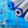 A glass of water and several water filter cartridges are arranged on a distressed blue wooden surface. Produktbild-Vorschau