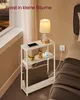 A small bedside table with a lamp, phone, and blanket, placed next to a bed. Produktbild-Vorschau