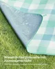 A picnic blanket with a checkered pattern is laid out on grass, showing its waterproof underside. Produktbild-Vorschau