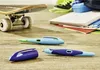 A collection of school supplies, including pens, a skateboard, and notebooks, arranged on a wooden surface. Náhľad obrázku produktu