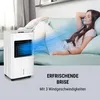 A woman relaxing on a sofa while a portable air cooler blows cool air on her. Produktbild-Vorschau