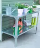 A metal garden table with various gardening items on it, including watering cans, plants, and boots. Voir les images du produit