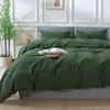 A neatly made bed with dark green bedding, a book, and dried flowers on top. Produktbild-Vorschau