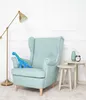 A blue dinosaur plush toy sits on a light blue armchair next to two small side tables. A floor lamp is to the left. Produktbild-Vorschau