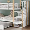 A close-up view of a white bunk bed with wooden accents, featuring a pull-out trundle bed and integrated storage stairs. Produktbild-Vorschau
