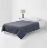 A gray weighted blanket is laid out on a bed next to a nightstand with a lamp and a pillow. Podgląd zdjęcia produktu