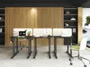 An office setting with three height-adjustable desks, each equipped with a laptop and a privacy screen. A green office chair is visible in the foreground. Produktbild-Vorschau