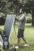 A man is standing next to a folded outdoor table tennis table in a grassy area with trees in the background. Produktbild-Vorschau