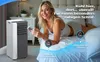 A woman is lying on a bed next to a portable air conditioner, holding a remote control. Produktbild-Vorschau