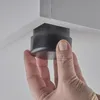 A hand is shown attaching a black furniture foot to the corner of a white surface. Produktbild-Vorschau