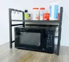 A black microwave oven is placed on a wooden surface, with a black metal shelf organizer on top. The shelf holds various items, including spice jars, bottles, and a box. Náhľad obrázku produktu