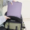 A person is placing a lavender laptop sleeve into a backpack. Náhled obrázku produktu