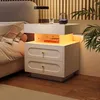 A modern white nightstand with two drawers and an open storage compartment with LED lighting, placed next to a bed in a bedroom setting. Podgląd zdjęcia produktu