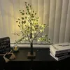 A decorative tree with LED lights sits on a dark surface next to books and a beaded necklace. Produktbild-Vorschau