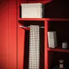 A shelf in a red cabinet with a storage box, a checkered scarf, and books. Náhľad obrázku produktu